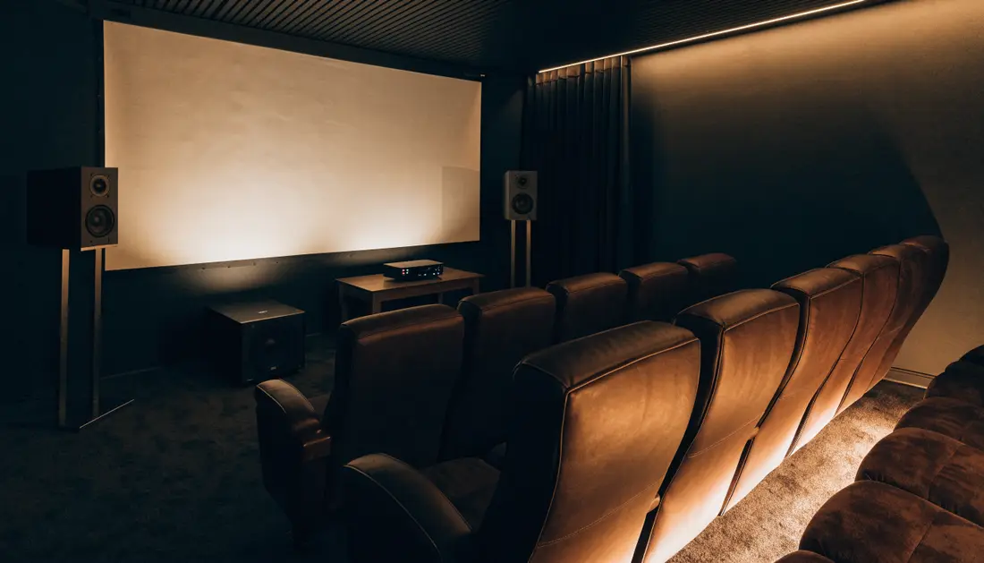 Dark home cinema room with a glowing screen, speakers and leather seats